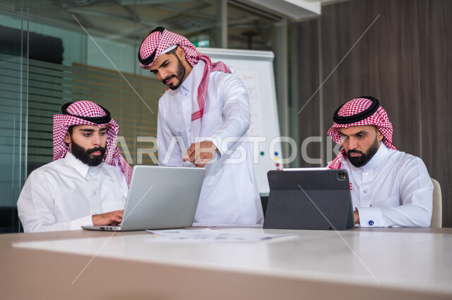 A group of Saudi Gulf businessmen meeting inside the company, using the laptop and tablet during the meeting, listening to the team leader, discussing the company’s goals and policy, explaining the business strategy, discussing a project, a workshop, trai