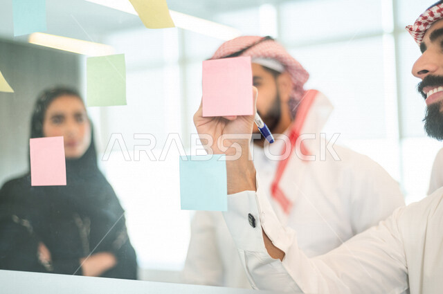 رجل عربي خليجي سعودي يدون الملاحظات والمهام على الورق ، فريق عمل خليجي سعودي يتشارك بتحديد الاهداف ، اجتماع داخل شركة سعودية ، انجاز مهام العمل ، تحقيق اهداف الشركة ، تطوير العمل
