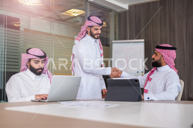 موظفان عربيان خليجيان سعوديان يتصافحان داخل الشركة ، اتفاق عمل بين رجال الاعمال ، صفقة ناجحة ، تعاون تجاري ، عمل جماعي مشترك