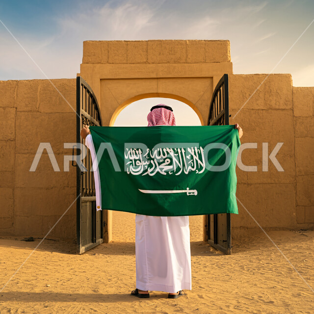 الفخر والاعتزاز بالهوية الوطنية، صورة من الخلف لرجل عربي خليجي سعودي يرتدي الثوب التقليدي والشماغ يقف باستقامة يحمل علم المملكة العربية السعودية، ذكرى العيد الوطني السعودي 23 مارس، يوم العلم السعودي 11 مارس، حب الوطن والانتماء إليه