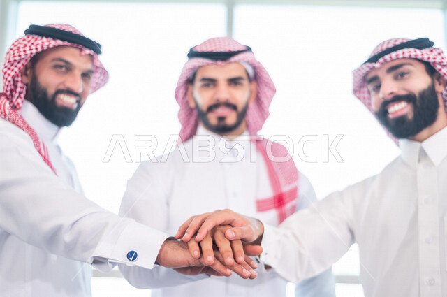 A picture of a Saudi Gulf work team putting their hands on top of each other, successful team work, unity and teamwork, accomplishing work tasks, achieving company goals, developing work