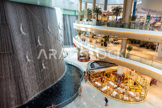  كشك لبيع العطور الفخمة، صورة من الأعلى لتماثيل فنية لغواصي اللؤلؤ وسط شلال داخل دبي مول، المعالم السياحية الترفيهية المشهورة في مدينة دبي، السياحة في الإمارات العربية المتحدة،  وجهات عائلية للتسوق، جذب واستقطاب السائحين من أنحاء العالم