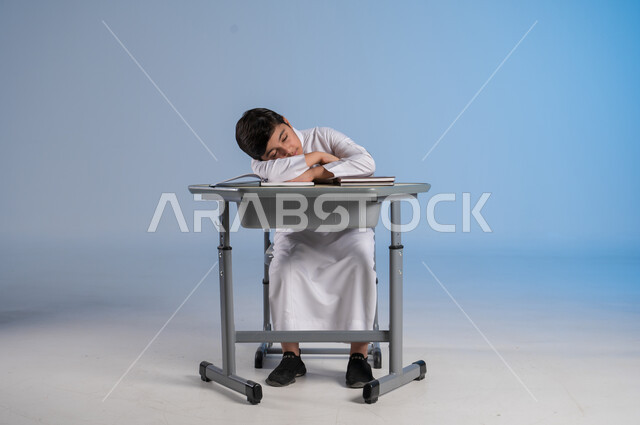 الشعور بالتعب والنعاس من الدراسة، متابعة المناهج الدراسية, بورتريه لفتى عربي خليجي سعودي يرتدي الثوب الأبيض التقليدي يجلس في مقعده ويأمامه مجموعة من الكتب, أهمية العلم والتعلم, خلفية زرقاء