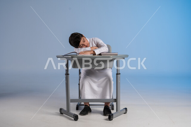 الشعور بالتعب والنعاس من الدراسة، متابعة المناهج الدراسية, بورتريه لفتى عربي خليجي سعودي يرتدي الثوب الأبيض التقليدي يجلس في مقعده ويأمامه مجموعة من الكتب, أهمية العلم والتعلم, خلفية زرقاء