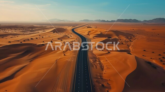 Urban development and growth in the deserts of the Kingdom of Saudi Arabia, an asphalt road extending along the desert, hills and sand dunes on the edges of the road in desert areas, facilitating movement between desert areas and cities, a paved road for the passage of cars and accelerating the movement of travelers