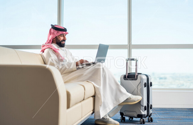 A Saudi Arabian Gulf businessman, getting work done through a laptop, getting ready to travel on a business trip, waiting hall at the airport, tourism and travel
