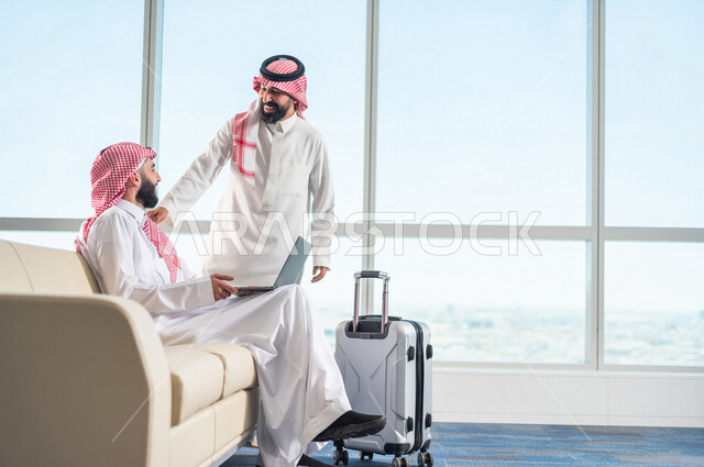رجل اعمال عربي خليجي سعودي، يلتقي بزميل العمل اثناء الجلوس في صالة الانتظار بالمطار، انجاز العمل من خلال جهاز الحاسوب المحمول،  الاستعداد للسفر في رحلة عمل، صالة الانتظار في المطار، سياحة وسفر