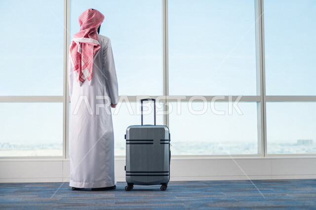 رجل أعمال عربي خليجي سعودي، يمسك بحقيبة السفر ويقوم بجرها، الاستعداد للسفر في رحلة عمل، صالة الانتظار في المطار، سياحة وسفر، قضاء أوقات ممتعة
