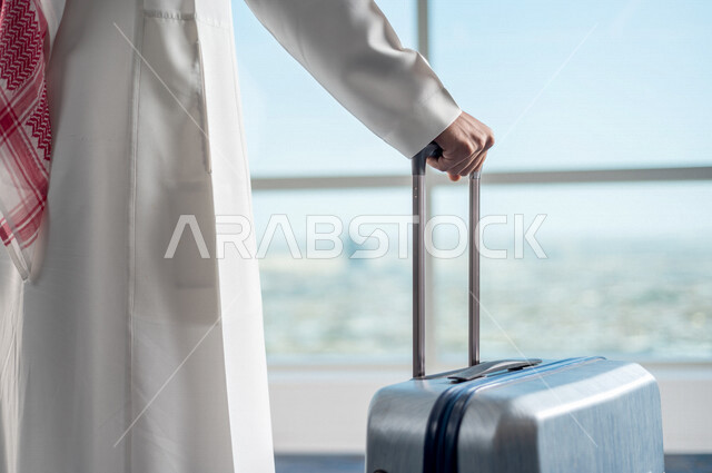 رجل أعمال عربي خليجي سعودي، يمسك بحقيبة السفر ويقوم بجرها، الاستعداد للسفر في رحلة عمل، صالة الانتظار في المطار، سياحة وسفر، قضاء أوقات ممتعة