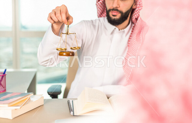 رجل عربي خليجي سعودي يعمل في مجال القضاء، امامه ميزان العدل، استلام قضية جديدة، يدرس اوراق القضية، يصافح احد موكليه