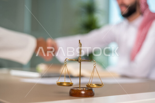 رجل عربي خليجي سعودي يعمل في مجال القضاء، امامه ميزان العدل، استلام قضية جديدة، يدرس اوراق القضية، يصافح احد موكليه