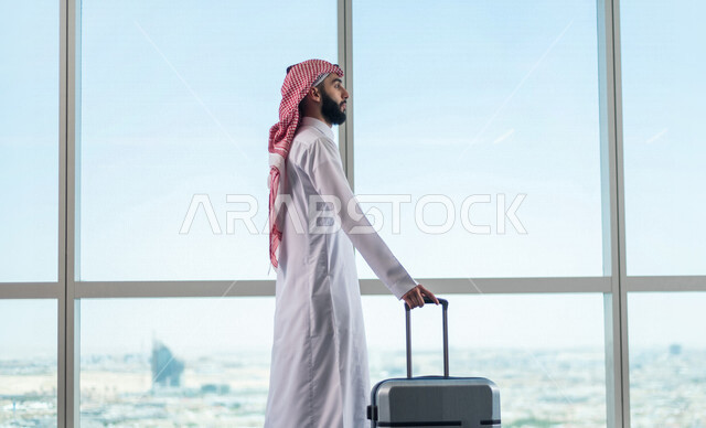 رجل أعمال عربي خليجي سعودي، يمسك بحقيبة السفر ويقوم بجرها، الاستعداد للسفر في رحلة عمل، صالة الانتظار في المطار، سياحة وسفر، قضاء أوقات ممتعة
