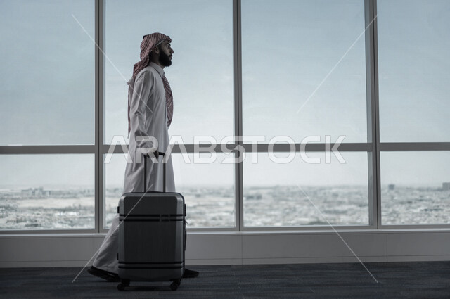 A Saudi Arabian Gulf businessman holding the travel bag and towing it, preparing to travel on a business trip, waiting lounge at the airport, tourism and travel, spending fun times