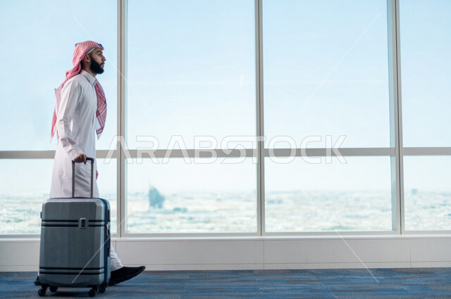 رجل أعمال عربي خليجي سعودي، يمسك بحقيبة السفر ويقوم بجرها، الاستعداد للسفر في رحلة عمل، صالة الانتظار في المطار، سياحة وسفر، قضاء أوقات ممتعة