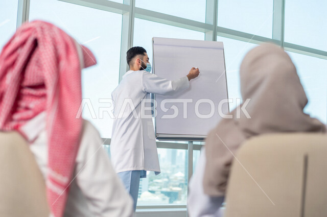 فريق طبي عربي خليجي سعودي، تبادل الاستشارات الطبية، العمل الجماعي للأطباء، ارتداء الكمامة، تقديم دورة، الشرح على لوح ابيض، مفهوم الطب والرعاية الصحية