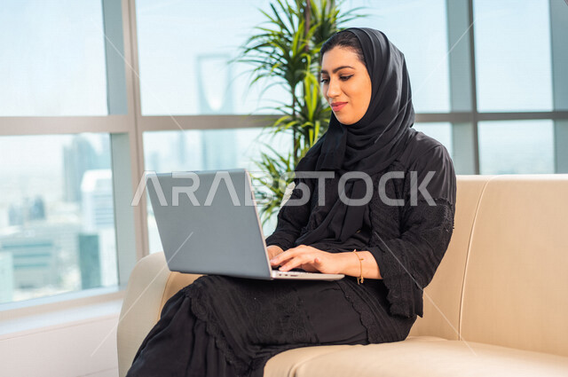 A Saudi Arabian Gulf businesswoman performs her work while she waits in the waiting room, get work done through her laptop, remote work meeting, online shopping