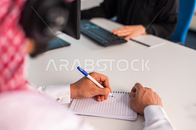 صوره مقربه  ليدين موظف  عربي سعودي خليجي يعمل في خدمة العملاء يرتدي  سماعة الاتصال , زملاء عمل في مركز الاستعلامات, اجراء اتصال فيديو من خلال الحاسوب , عقد اجتماع عمل عبر الانترنت , العمل عن بعد , متابعة وتطوير العمل
