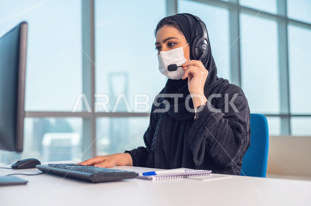 موظفه عربيه سعوديه خليجيه تعمل في خدمة العملاء ترتدي سماعة الاتصال, استعلامات واستفسارات, الاجابه على اسئلة العملاء, اجراء اتصال فيديو من خلال الحاسوب , عقد اجتماع عمل عبر الانترنت, العمل عن بعد , متابعة وتطوير العمل الالتزام بالاجراءات الوقائيه