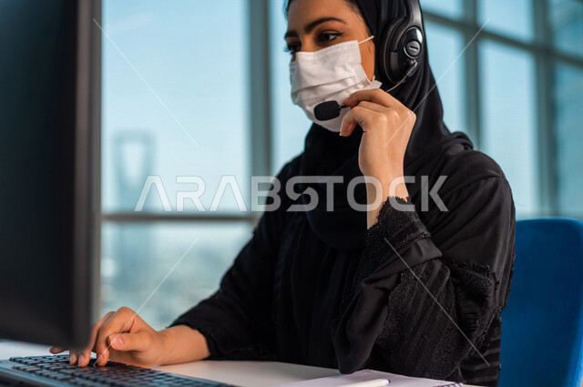 موظفه عربيه سعوديه خليجيه تعمل في خدمة العملاء ترتدي سماعة الاتصال, استعلامات واستفسارات, الاجابه على اسئلة العملاء, اجراء اتصال فيديو من خلال الحاسوب , عقد اجتماع عمل عبر الانترنت, العمل عن بعد , متابعة وتطوير العمل الالتزام بالاجراءات الوقائيه