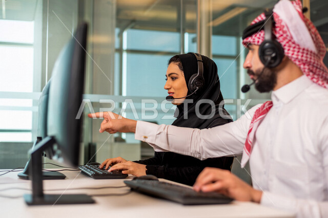 موظفان عربيان سعوديان خليجيان يعملان في خدمة العملاء في شركه يرتديان سماعة الاتصال, استعلامات واستفسارات, الاجابه على اسئلة العملاء, اجراء اتصال فيديو من خلال الحاسوب , عقد اجتماع عمل عبر الانترنت, العمل عن بعد , متابعة وتطوير العمل , مناقشة عمل, ارشاد وت