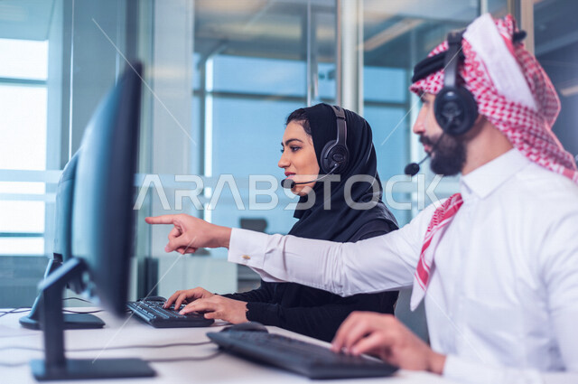 موظفان عربيان سعوديان خليجيان يعملان في خدمة العملاء في شركه يرتديان سماعة الاتصال, استعلامات واستفسارات, الاجابه على اسئلة العملاء, اجراء اتصال فيديو من خلال الحاسوب , عقد اجتماع عمل عبر الانترنت, العمل عن بعد , متابعة وتطوير العمل , مناقشة عمل, ارشاد وت