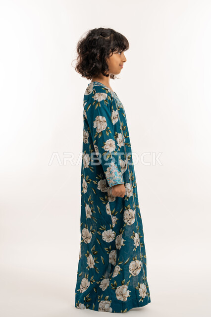 Self-confidence gestures, love of adornment and wearing new clothes, concept of elegance and softness, interest in external appearance, side portrait of an Arab Gulf Emirati girl wearing an Eid dress, elegant Saudi girl standing straight, full body photo, white background