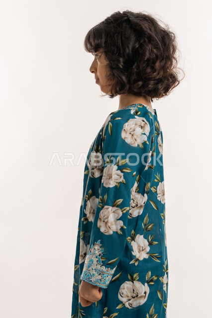 The concept of elegance and softness, interest in external appearance, love of adornment and wearing new clothes, side portrait of an Arab Gulf Emirati girl wearing an Eid dress, an elegant Saudi girl standing straight, white background