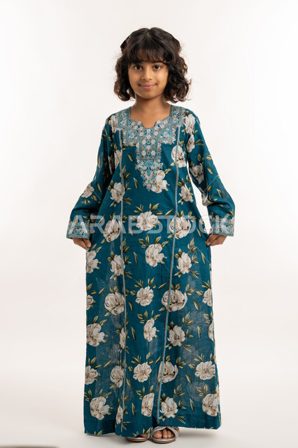 النظر الى الكاميرا بايماءات الثقة بالنفس، حب التزين وارتداء الملابس الجديدة، مفهوم الاناقة والنعومة، الاهتمام بالمظهر الخارجي، بورتريه لفتاة عربية خليجية اماراتية ترتدي فستان العيد تمسك بطرف ثوبها بتعابير السرور، بنت سعودية انيقة تقف باستقامة، صورة لكامل الجسم، خلفية بيضاء