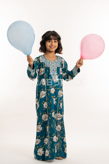 Children's joy and happiness on Eid, looking at the camera with expressions of pleasure and happiness, celebrating religious holidays and occasions, portrait of an Arab Gulf Emirati girl wearing a girl's jalabiya holding colorful balloons in her hand, a Saudi girl standing with gestures of joy, full body photo, white background