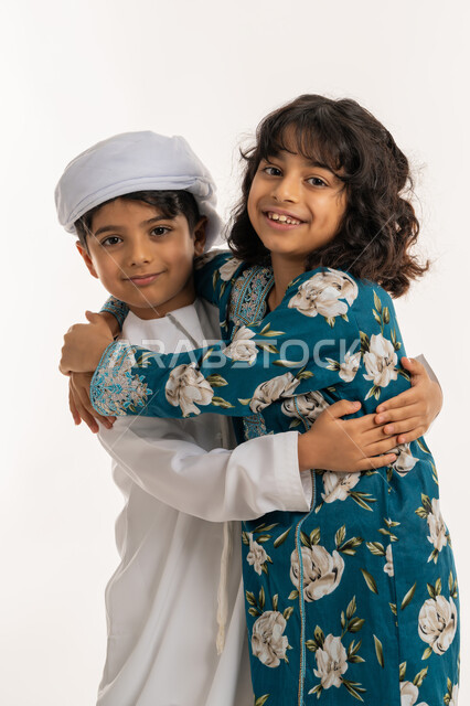 مفهوم المودة بين الاخوة, قضاء اوقات ممتعة مع العائلة، بورتريه لشقيقين عربيين خليجيين اماراتيين مبتسمان يعانقان بعضهما بإيماءات السعادة و الفرح, تقوية وتعزيز الروابط الاسرية, خلفية بيضاء