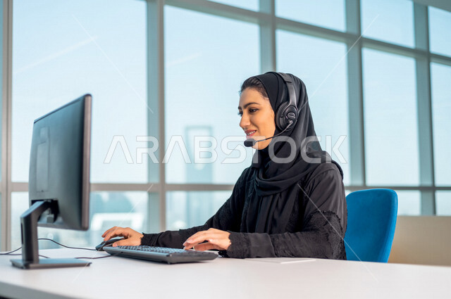 موظفه عربيه سعوديه خليجيه تعمل في خدمة العملاء ترتدي سماعة الاتصال, استعلامات واستفسارات, الاجابه على اسئلة العملاء, اجراء اتصال فيديو من خلال الحاسوب , عقد اجتماع عمل عبر الانترنت, العمل عن بعد , متابعة وتطوير العمل .