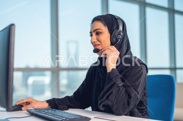 موظفه عربيه سعوديه خليجيه تعمل في خدمة العملاء ترتدي سماعة الاتصال, استعلامات واستفسارات, الاجابه على اسئلة العملاء, اجراء اتصال فيديو من خلال الحاسوب , عقد اجتماع عمل عبر الانترنت, العمل عن بعد , متابعة وتطوير العمل .