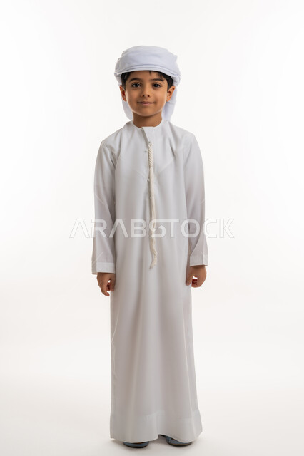 الاهتمام بالأناقة والمظهر الخارجي، تعابير الجدية والثقة بالنفس، بورتريه لولد عربي خليجي اماراتي مبتسم يرتدي االعمامة والكندورة ينظر الى الكاميرا بإيماءات الحزم والسرور، صورة الجسم بالكامل، خلفية بيضاء