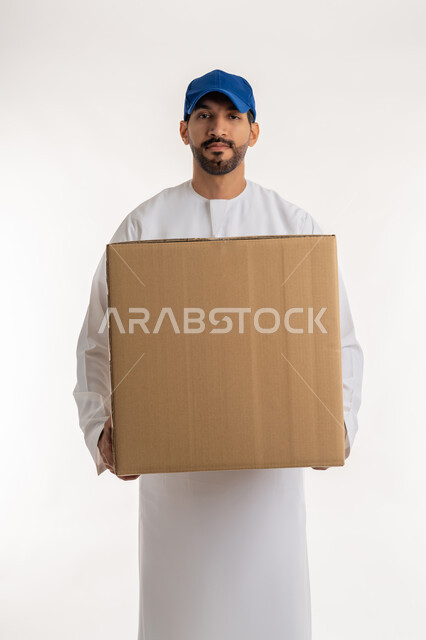 Services and shipping High quality delivery, customer order delivery process, online shopping and ordering products, portrait of a young Arab Gulf Emirati man wearing a kandura and a blue cap holding a cardboard box, white background