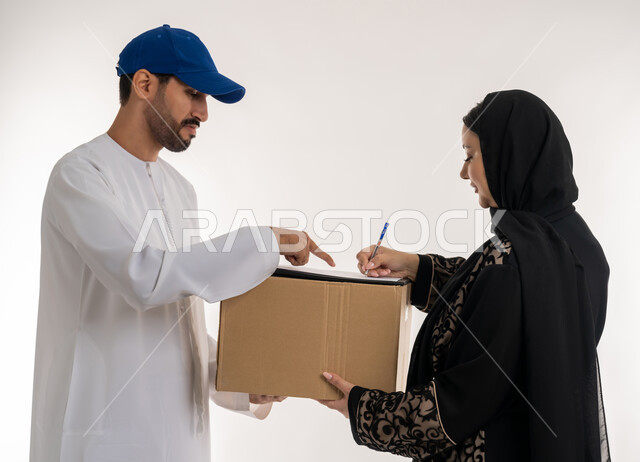 دمج العمل مع التقنية والتكنولوجيا، شبكات التوصيل الاونلاين في الخليج، التسوق وطلب المنتجات عبر الإنترنت, بورتريه لشاب عربي خليجي اماراتي يرتدي الزي الكاجوال و القبعة الزرقاء يقوم بتوثيق استلام الطرود يقف بجانب امرأة عربية خليجية امارتيه ، خلفيه بيضاء