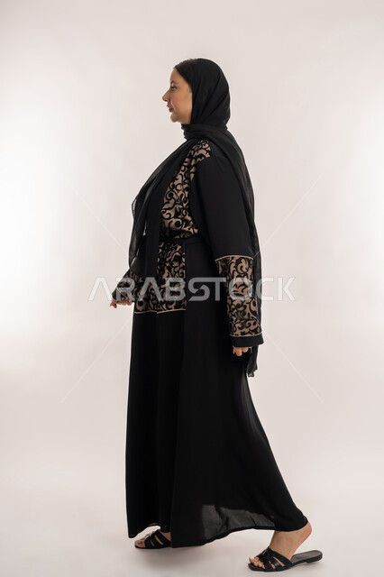 Standing Up Straight and Self-Pride, Taking Care of Appearance, Side Portrait of a Veiled Emirati Gulf Arab Woman Wearing a Black Abaya Standing with Gestures of Firmness and Seriousness, Full-Length Body, White Background