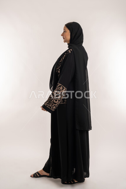 الوقوف باستقامة والاعتزاز بالنفس, الاهتمام بالمظهر الخارجي, بورتريه من الجانب لامرأة عربية خليجية اماراتية محجبة ترتدي العباءة السوداء تقف بايماءات الحزم والجدية، الجسم بالطول الكامل، خلفية بيضاء