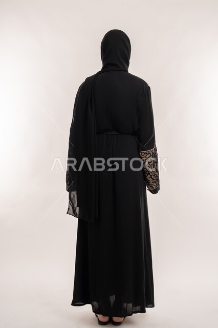 مفهوم الاناقه و الاهتمام بالمظهر الخارجي، بورتريه من الخلف لإمرأة عربية خليجية اماراتية محجبة ترتدي العباءة السوداء تقف باستقامة واستعداد، صورة الجسم بالطول الكامل، خلفية بيضاء