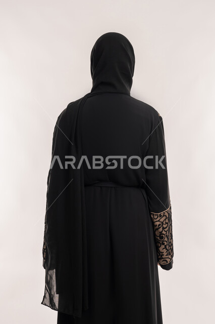 مفهوم الاناقه و الاهتمام بالمظهر الخارجي، بورتريه من الخلف لإمرأة عربية خليجية اماراتية محجبة ترتدي العباءة السوداء تقف باستقامة واستعداد، خلفية بيضاء