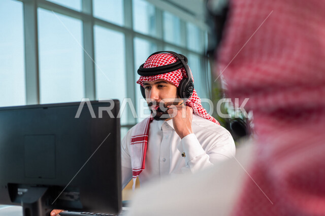 موظفان عربيان سعوديان خليجيان يعملان في خدمة العملاء في شركه يرتديان سماعة الاتصال, استعلامات واستفسارات, الاجابه على اسئلة العملاء, اجراء اتصال فيديو من خلال الحاسوب , عقد اجتماع عمل عبر الانترنت, العمل عن بعد , متابعة وتطوير العمل .