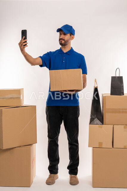 استخدام الاجهزة و التقنيات الحديثة المتطورة, التسوق و طلب المنتجات عبر الإنترنت، إستلام المشتريات و تسليم البضائع للزبائن بالوقت المحدد و بشكل سليم، بورتريه لشاب عربي خليجي اماراتي يرتدي الكندورة و الطاقية يحمل بيده صنوق كرتوني، الجسم بالطول الكامل, خلفية بيضاء