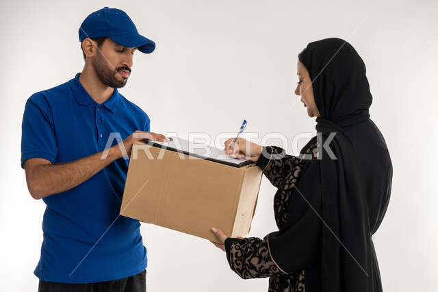 شبكات التوصيل الاونلاين في الخليج، دمج العمل مع التقنية والتكنولوجيا، التسوق وطلب المنتجات عبر الإنترنت, بورتريه لشاب عربي خليجي اماراتي يرتدي الزي الكاجوال و القبعة الزرقاء يقف بجانب امرأة عربية خليجية امارتيه تقوم بتوثيق استلام الطرود، خلفيه بيضاء