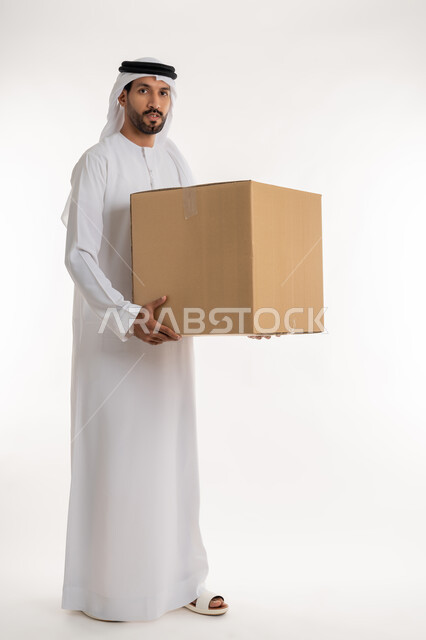 High quality shipping and delivery services, online shopping and ordering, customer delivery process, portrait of a young Emirati Gulf Arab man wearing a kandura and ghutra looking at the camera holding a cardboard box, full body, white background