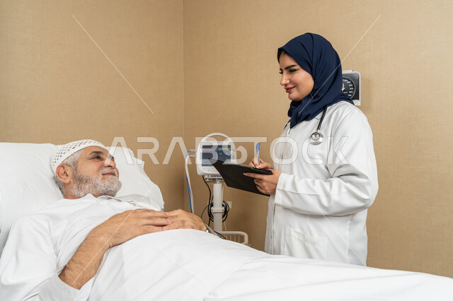 تقديم الخدمات والاستشارات الطبية للمراجعين، مفهوم الطب والرعاية الصحية، طبيبة عربية خليجية اماراتية ترتدي الحجاب والمعطف الابيض تقوم بتدوين معلومات مريض مسن عربي اماراتي مستلقي على السرير، مهن ووظائف نسائية، دراسة و مراجعة حالات المرضى