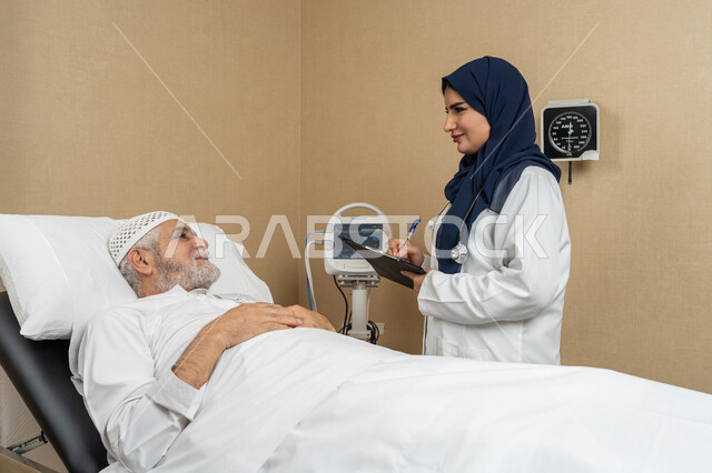 تقديم الخدمات والاستشارات الطبية للمراجعين، مفهوم الطب والرعاية الصحية، طبيبة عربية خليجية اماراتية ترتدي الحجاب والمعطف الابيض تقوم بتدوين معلومات مريض مسن عربي اماراتي مستلقي على السرير، مهن ووظائف نسائية، دراسة و مراجعة حالات المرضى