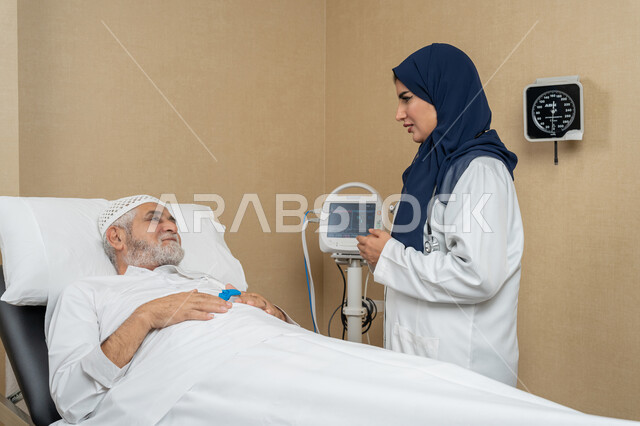 تقديم الخدمات والاستشارات الطبية للمراجعين، مفهوم الطب والرعاية الصحية، طبيبة عربية خليجية اماراتية ترتدي الحجاب والمعطف الابيض تقوم بتبادل الاحاديث والمعلومات مع مريض مسن عربي اماراتي مستلقي على السرير، مهن ووظائف نسائية، دراسة و مراجعة حالات المرضى
