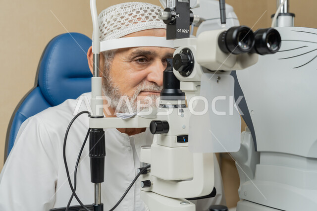 Diagnosis and identification of visual problems, close-up of an elderly Emirati Gulf Arab man wearing a ghutra sitting on a chair examining his eyes with an ophthalmoscope, assessing vision and detecting eye diseases, the concept of services and health care in hospitals and centers, using modern advanced devices