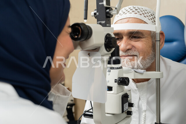 استخدام الأجهزة الحديثة المتطورة، تشخيص وتحديد المشاكل البصرية، صورة مقربة لطبيبة عربية خليجية اماراتية تقوم بفحص عيني رجل مسن اماراتي عربي خليجي بجهاز المنظار العيني، تقييم مدى الرؤية والكشف عن الامراض العينية، مفهوم الخدمات والرعاية الصحية في المشافي والمراكز الطبية