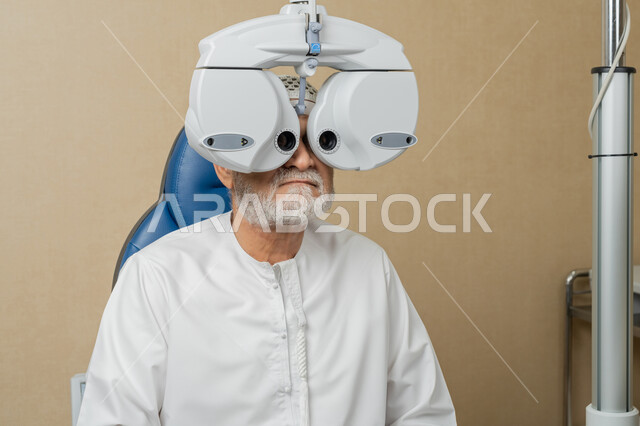 تشخيص وتحديد المشاكل البصرية، صورة مقربة لرجل مسن عربي اماراتي خليجي يرتدي الغترة امام جهاز الفحص البصري للتأكد من صحة النظر، تقييم مدى الرؤية والكشف عن الامراض العينية، مفهوم الخدمات والرعاية الصحية في المستشفيات والمراكز، استخدام الأجهزة الحديثة المتطورة