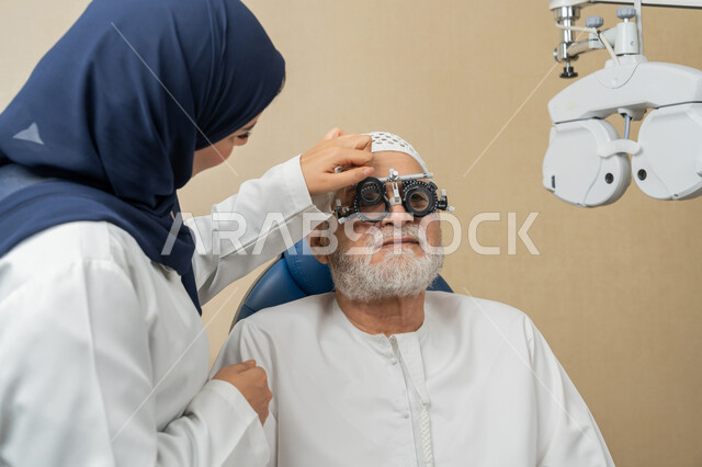 Using advanced modern devices, diagnosing and identifying visual problems, a close-up image from the side of an Arab Gulf Emirati female doctor examining the eyes of an elderly Emirati Arab Gulf man with an ophthalmoscope, assessing the extent of vision and detecting eye diseases, the concept of services and health care in hospitals and medical centers